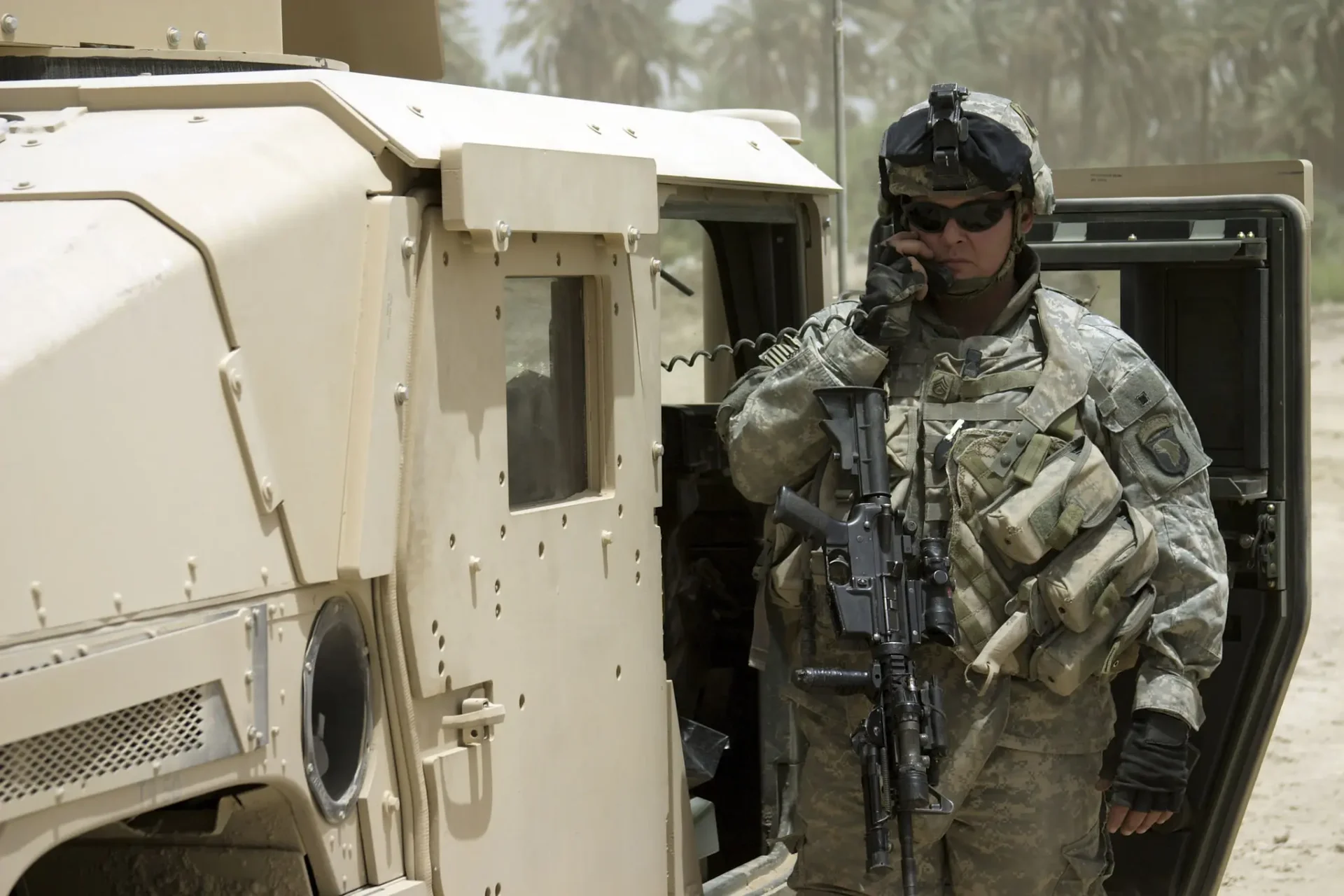 Soldier standing guard by a military vehicle in desert terrain.
